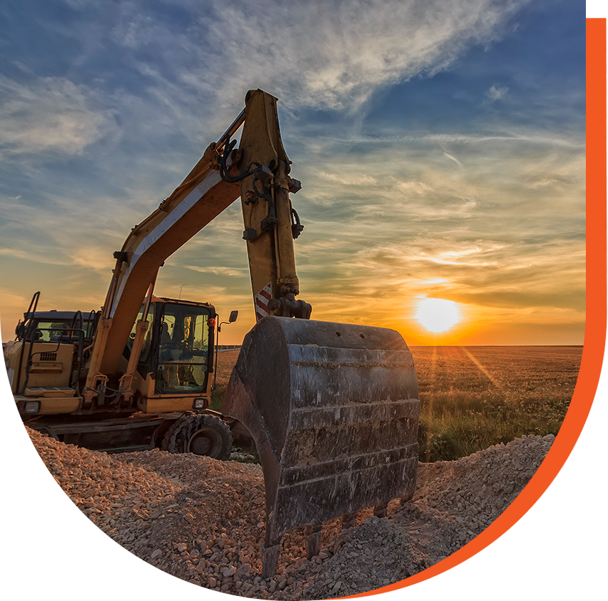 An excavator on a pile of gravel at sunset, with a clear sky and sun setting on the horizon.